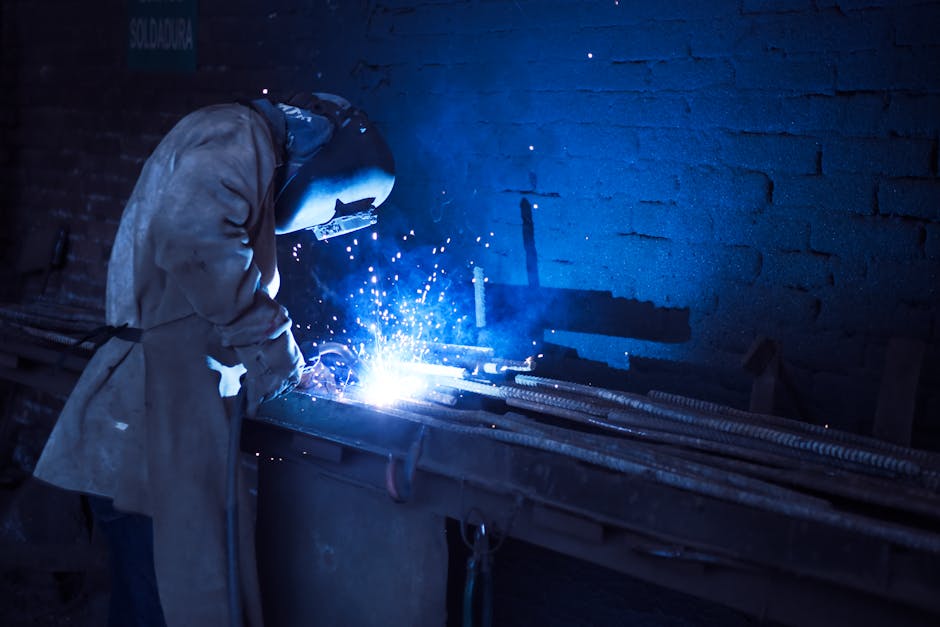 Industrial worker welding metal indoors, emitting bright blue sparks and smoke.